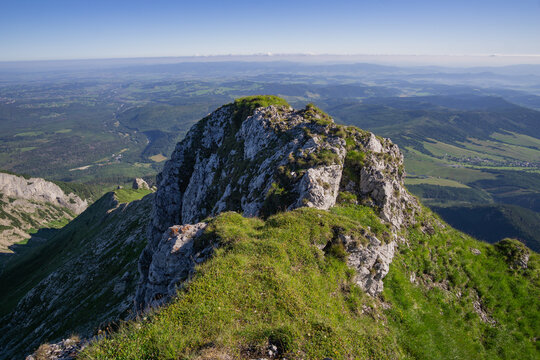 View of rugged, rocky peak with patches of vibrant green grass contrasting against the backdrop of hazy, distant mountains, Havran, Presov Region, Slovakia.