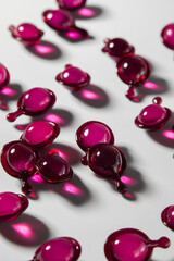 Scattered pink and purple serum capsules with dramatic shadows on a white background