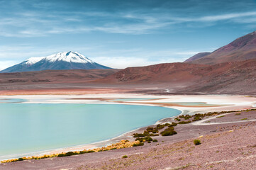 High-altitude lagoon with turquoise water and salt surface in Altiplano plateau, Bolivia. Volcanoes with snow in the background.