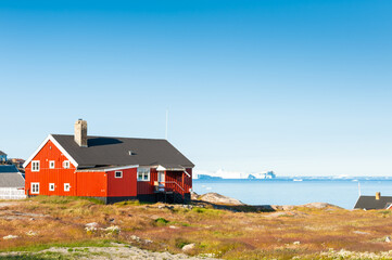 Ilulissat, western Greenland. Colorful houses on the shore of Atlantic ocean. Big icebergs floating in the icefjord.