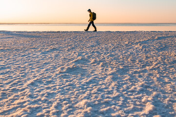 Man traveler with backpack walking on the salt lake at sunrise.