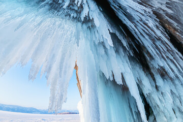 Ice cave with icicles in Baikal lake at sunset. Icicles on the rocks. Winter landscape of Baikal lake, Russia