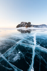 Blue transparent cracked ice on Baikal lake in winter. Sunrise at Khoboy cape of Olkhon island, Baikal, Russia.