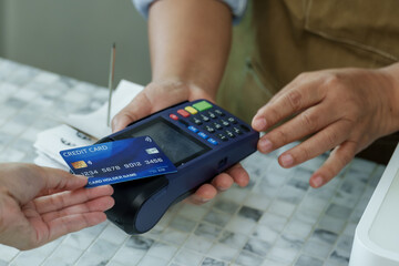 Close view of credit card reaching toward payment terminal at coffee shop, barista assisting customer with seamless cashless transaction in cozy small family-owned cafe, Concept small business