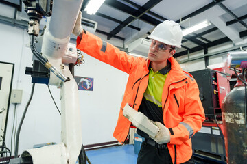 Asian male engineer adjusting robotic arm in advanced automation training facility focusing on precision control and smart manufacturing process using industrial technology for upskilling workforce
