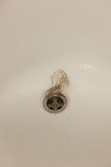 Water drain hole of a bathtub is clogged with long hair clump. Closeup.