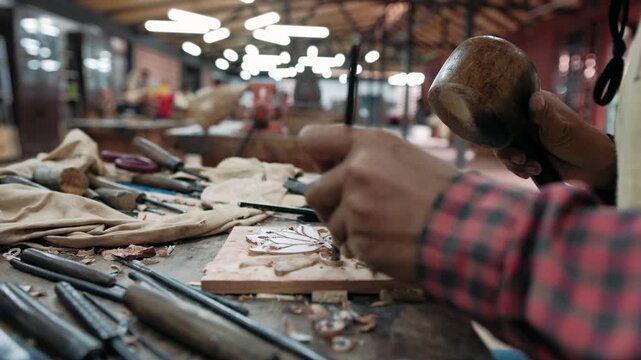 Close up of a carpenter using a chisel and mallet to carefully carve an intricate design into a wooden plank in a workshop, Siem Reap, Cambodia.