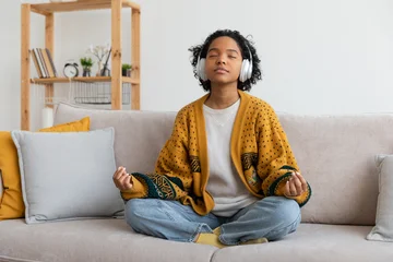 Fototapete Rund Lotusblume Yoga mindfulness meditation. Young healthy African girl practicing yoga at home. Woman sitting in lotus pose on couch meditating smiling relaxing indoor. Girl doing breathing practice. Yoga at home  © Юлия Завалишина