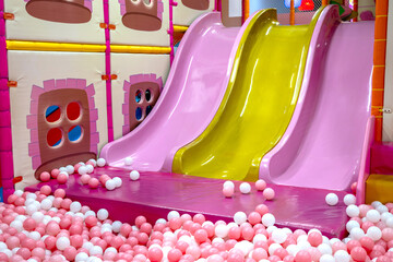 Colorful indoor playground with pink and yellow slides surrounded by pink-white ball pit, creating a bright and playful childrens environment