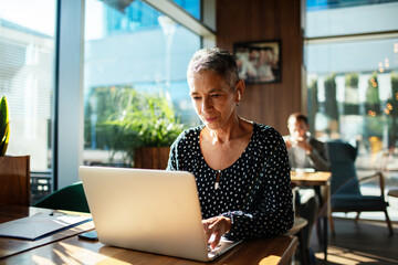 Mature woman focused on laptop in modern cafe