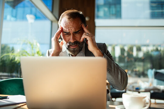 Mature man stressed with headache at laptop in cafe
