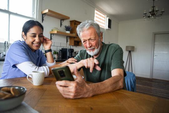 Adult caregiver helping confused senior man with smartphone at home