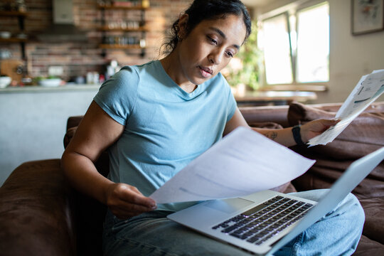 Young adult woman looking concerned while reviewing bills at home