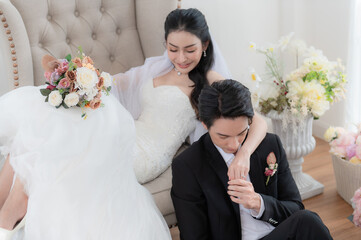 Happy Asian bride and groom in wedding attire, posing indoors with clean background. Stylish groom portrait for wedding photography concept.