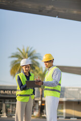 Obraz premium Professional engineers wearing safety helmets are reviewing blueprints on a tablet and discussing manufacturing projects with colleagues, emphasizing safety, teamwork, planning, and industry 
