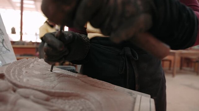 Close up of hands carve a traditional khmer apsara bas relief on stone in a workshop, using a chisel and mallet. Siem reap, Cambodia.