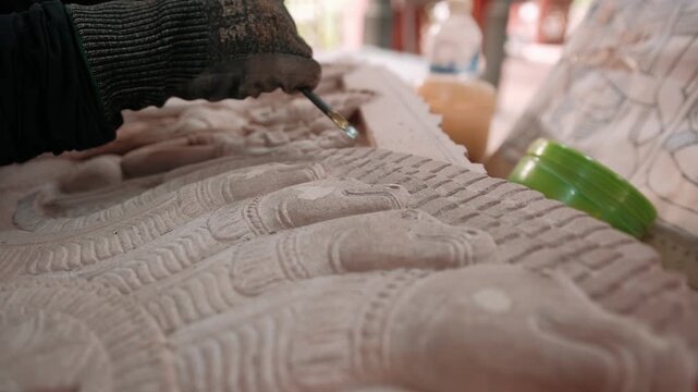 Close up of hands carve a traditional khmer apsara bas relief on stone in a workshop, using a chisel and mallet. Siem reap, Cambodia.