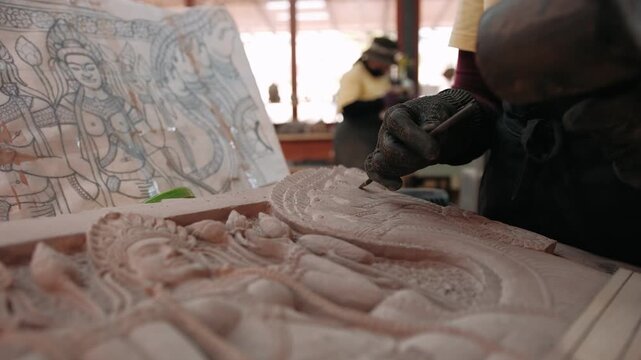 Close up of hands carve a traditional khmer apsara bas relief on stone in a workshop, using a chisel and mallet. Siem reap, Cambodia.