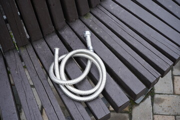 Metal hose lies on a wooden bench background.