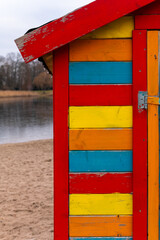 Colorful beach hut stands by the tranquil lake under a cloudy sky during an overcast afternoon