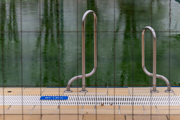 Calm waters beckon near the poolside with gleaming metal handrails under a tranquil sky