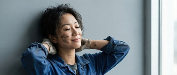 Asian woman worker, dirty face, resting with hands behind head, satisfied smile, blue work shirt, gloves, indoors, daylight Concept of hard work, achievement, and satisfaction