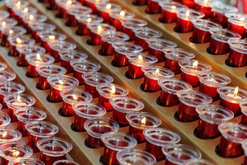 Rows of red votive candles burning with warm glowing flames in a church, symbol of prayer, remembrance, spirituality, meditation, and religious devotion