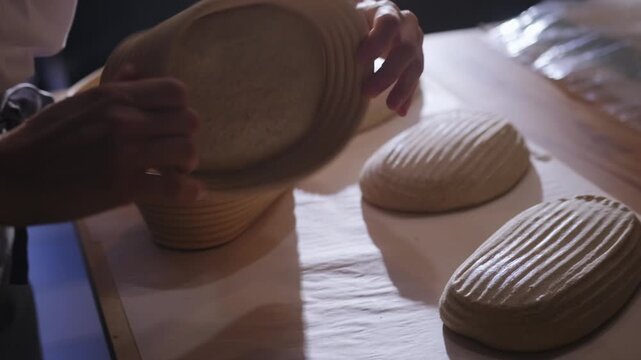 A baker inverts proofing baskets and places the formed dough on the counter before baking tartines. Manual fermentation, a professional process, the texture of raw dough, traditional baking.