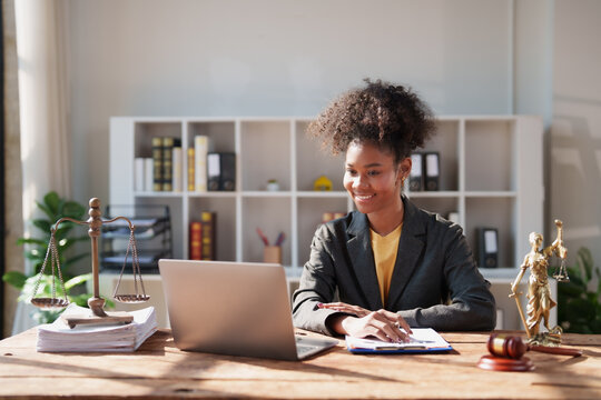 Young African American woman lawyer smiling at laptop while preparing legal documents and researching cases in a professional law firm office, confident and focused