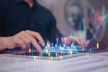 Businessman using computer laptop and digital tablet working in home office with virtual investment stock data charts in concept of investment financial business marketing and plans