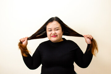 Plus-size woman with long dark hair pulling strands, looking stressed, white background