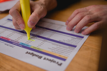 Person hand usesing a yellow highlighter pen to mark specific numbers on a printed document. This process involves reviewing and emphasizing key figures within a financial report or data sheet