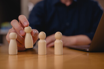 Choosing the Right Candidate Employee Selection Process. Businessman leader holding and choosing wooden people from a group of employees while working on laptop computer in office
