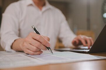 Businessman using pen and business data sheet and computer laptop on tablet to analysis graph company financial budget report and cost work progress and planning for future in office room
