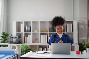 Asian female medical professional wearing blue scrubs and stethoscope, engaging in an online consultation with a patient via laptop in a modern healthcare setting