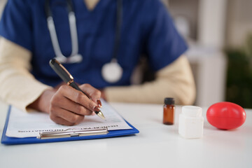 Healthcare professional in blue scrubs with stethoscope filling out patient medical forms on a...