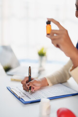 Fototapeta premium Doctor writing medical patient form on clipboard while holding amber medicine bottle, providing healthcare consultation and treatment in clinic office