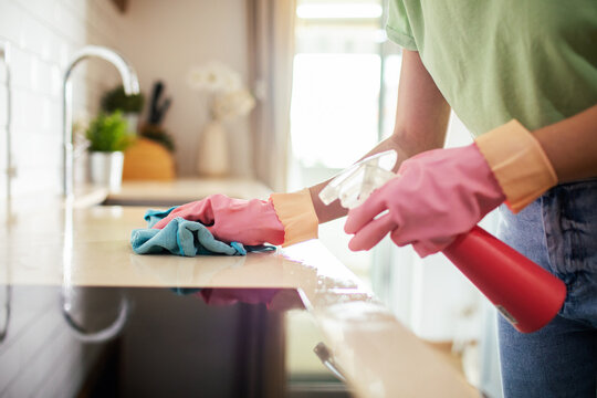 Adult cleaning kitchen countertop with spray, focused at home kitchen
