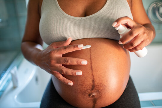 Adult woman calmly applying belly lotion in bathroom