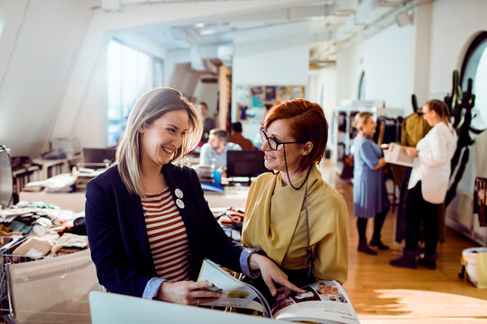 Adult coworkers smiling while reviewing fashion catalog in creative studio