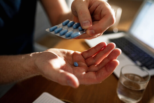 Adult calmly taking blue pill at home office desk