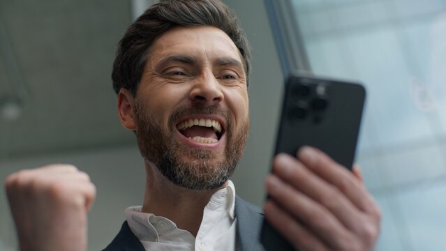 Close up happy smiling Caucasian middle-aged business man winning with mobile phone online bet casino success victory in office excited businessman male manager employer satisfied with smartphone win