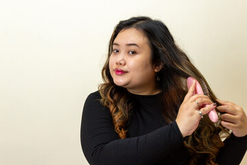 Young woman brushing her long wavy hair with a pink comb, looking at camera