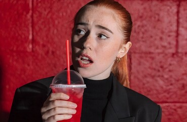 Red Expression Concept &ndash; Person in Black Outfit Holding Red Drink with Straw Against Red Brick Wall, lifestyle, emotion, drink, red, straw, brick wall, black outfit, red hair, beverage, expression