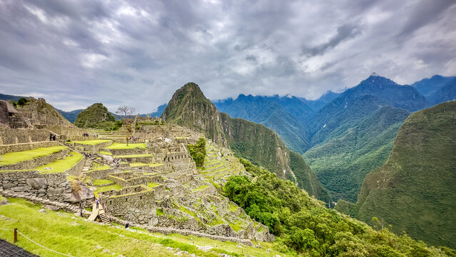 View of ancient stone terraces cascading down the mountainside, blending with the verdant landscape under a dramatic sky, Machu Picchu, Peru.
