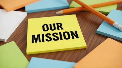 Yellow sticky note clearly displaying the bold black phrase our mission surrounded by colorful stationery and writing utensils on a wooden desk surface