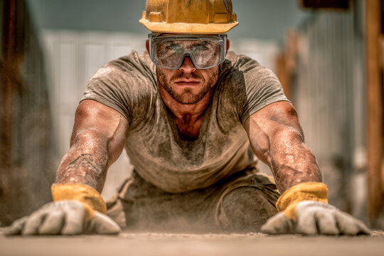 Determined construction worker wearing safety helmet and goggles stretching forward while covered in dust and dirt on an active building site environment