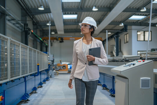 Female manager supervises production in a metal manufacturing plant while workers collaborate on the factory floor.
