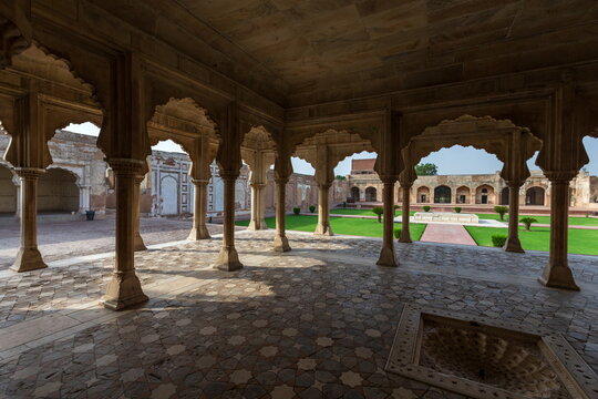 View of ornate arched colonnades framing a lush green courtyard with geometric patterns underfoot, bathed in warm light, Lahore, Punjab, Pakistan.