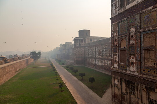 View of ancient walls adorned with intricate patterns, a lush green lawn, and a misty pathway evoking historical depth, Lahore Fort, Punjab, Pakistan.